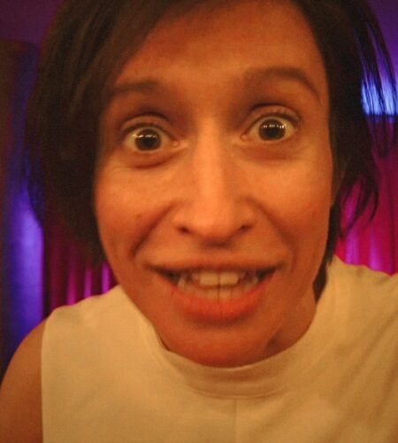 A dark-haired woman in close up, with an expression somewhere between smile and grimace.