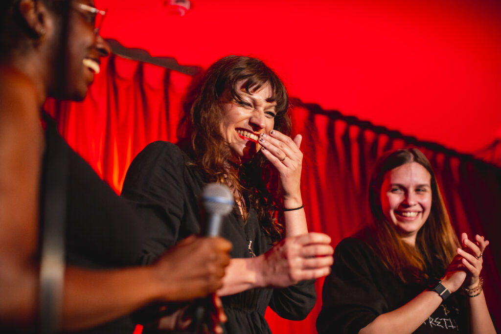 Josie Kikas laughs on stage between Mitsy Chanel-Blot and Anastasia.